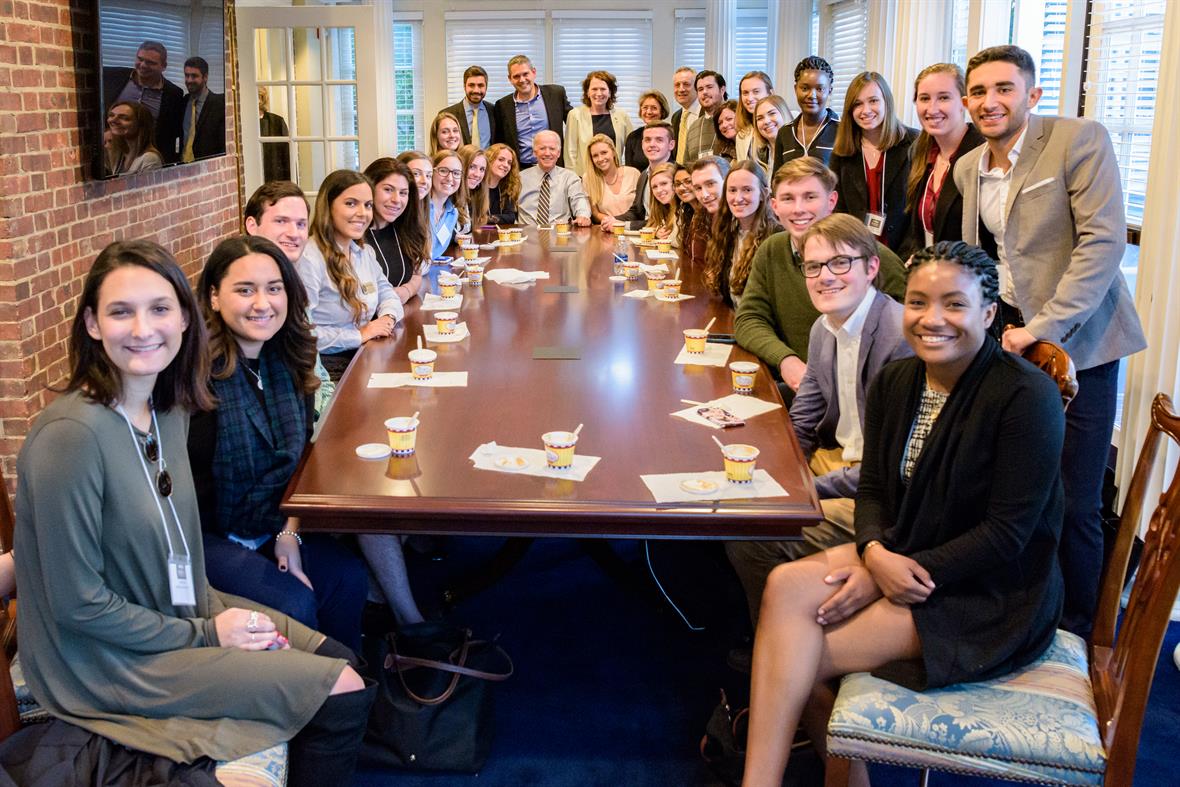 Students posing for a photo with President Biden around the conference room table at the Biden Institute
