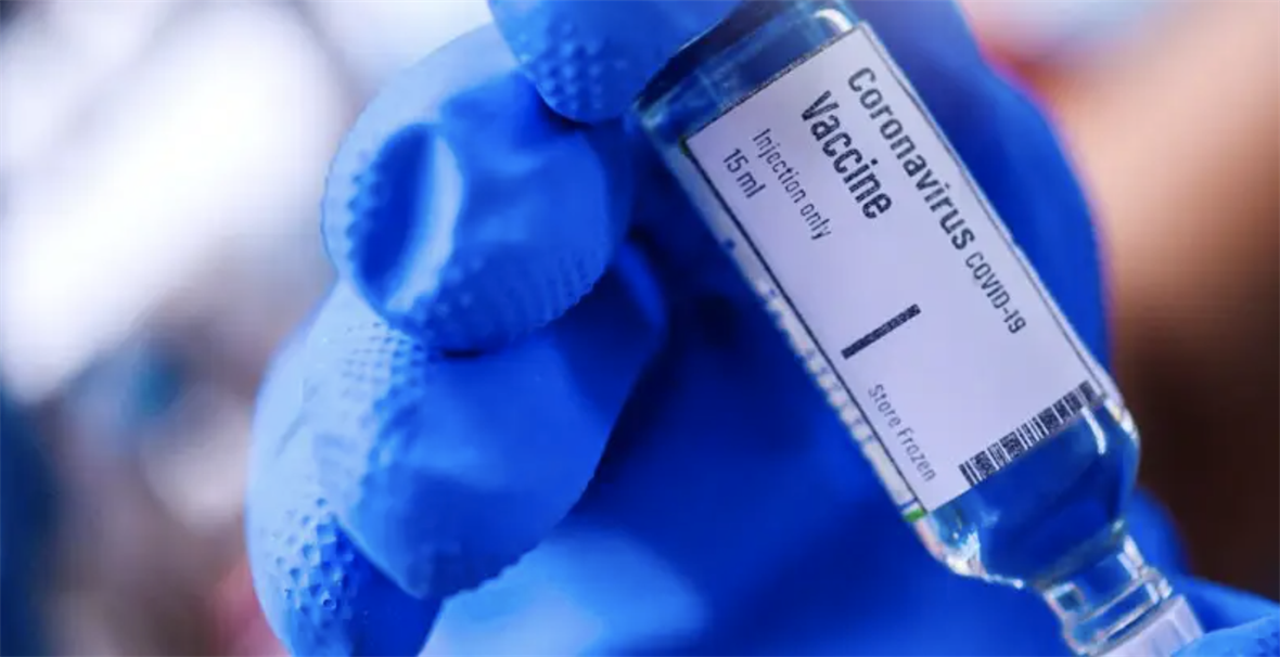 A hand in a blue glove holds a vial of coronavirus vaccine.