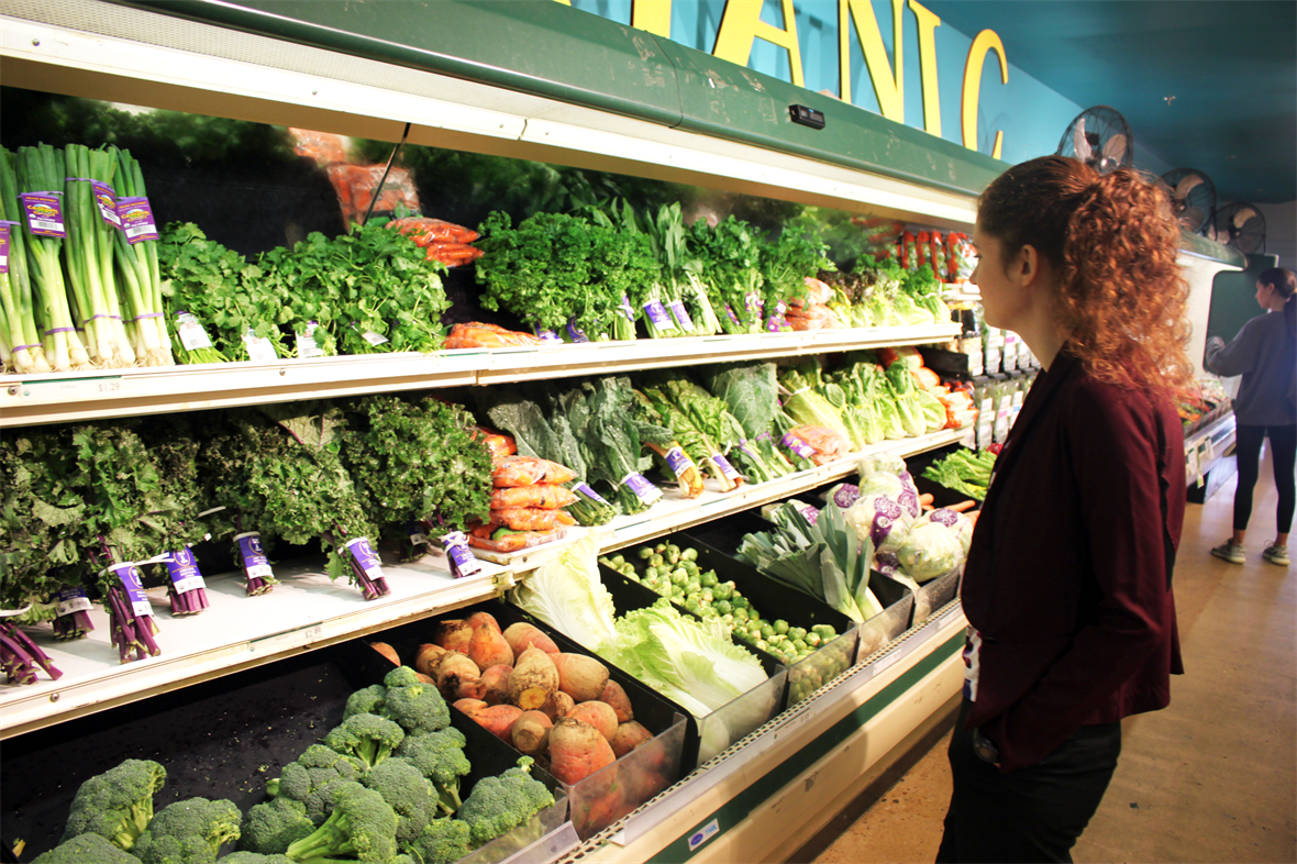 Female student looks at produce options at a grocery store.