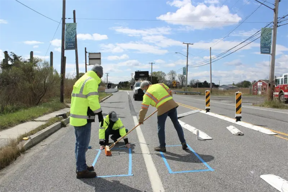 Three people painting on the surface of a road.