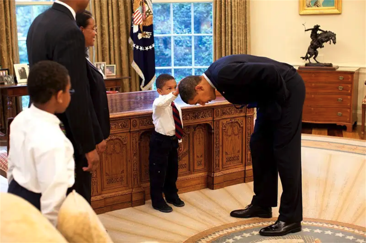 President Barack Obama bends down to allow a young boy to touch his hair.