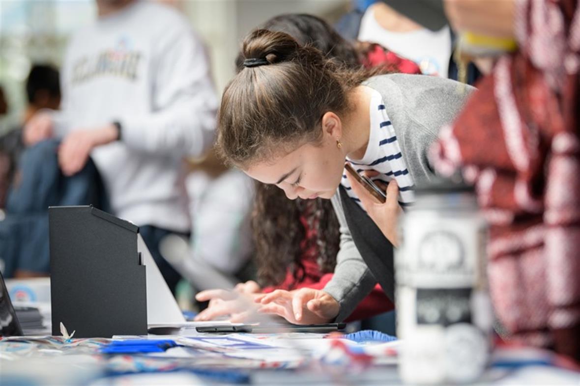 A young woman leans over a table to complete her voter registration.