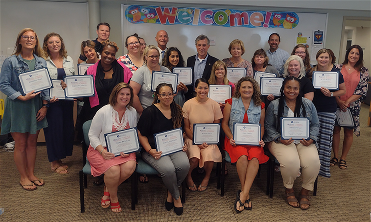 Twenty four teachers hold their certificates with Gov. Carney and Secretary of State Bullock smiling in the middle of the photo. 