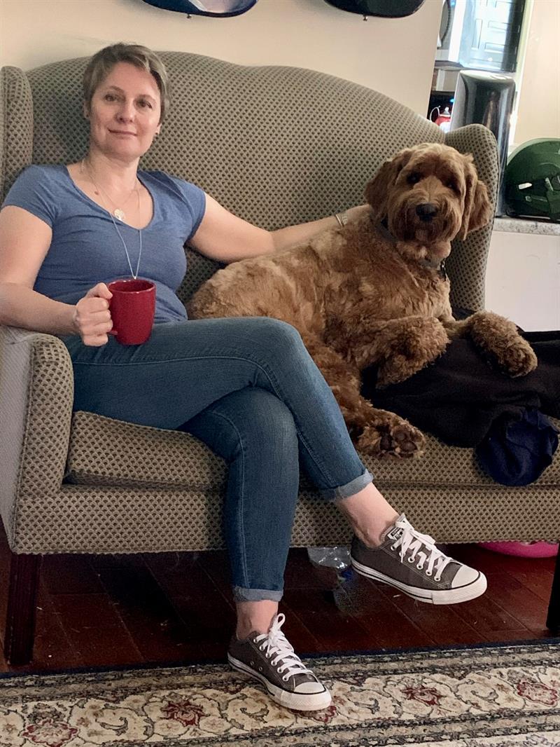 A portrait of Marta Driscoll and her pet dog sitting on a brown couch. 