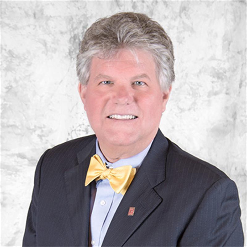 Phil McGinnis smiles wearing a yellow bow tie and a navy suit.