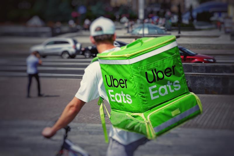 An Uber Eats driver rides on a bicycle carrying a food warmer. Photo credit: Robert Anasch/Unsplash